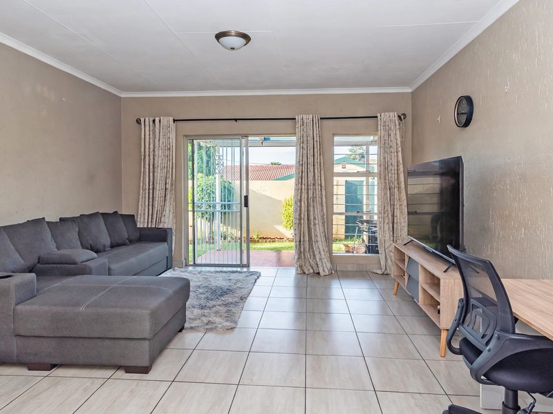 A bright living room featuring tiled flooring, a sliding glass door with security gate, and direct access to the rear patio area.