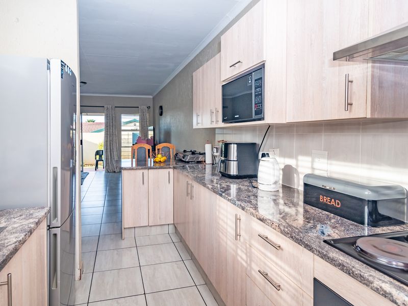 A functional kitchen featuring light wood-finish cabinetry, granite countertops, built-in microwave, and extractor fan, with tiled flooring leading toward an open-plan living area.