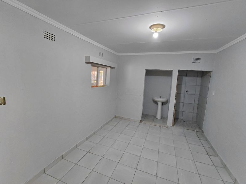 A basic, empty bathroom featuring a pedestal basin and a partially finished tiled shower area with neutral floor tiling.