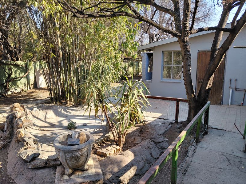 Rear garden area featuring a paved walkway, metal fencing, and established landscaping with a stone garden feature and exterior building access.