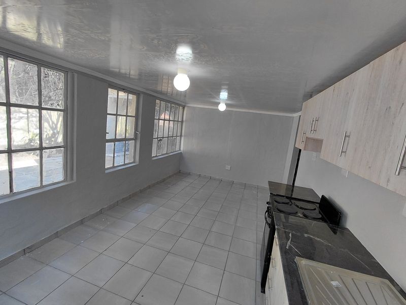 A bright, empty kitchen featuring tiled flooring, built-in cabinetry, an electric hob, and large windows providing ample natural light.