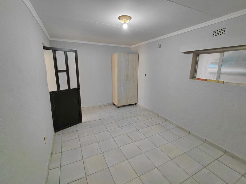 A simple, empty bedroom featuring tiled flooring, a metal-framed door, and a small sliding window, providing a blank canvas for potential interior design.