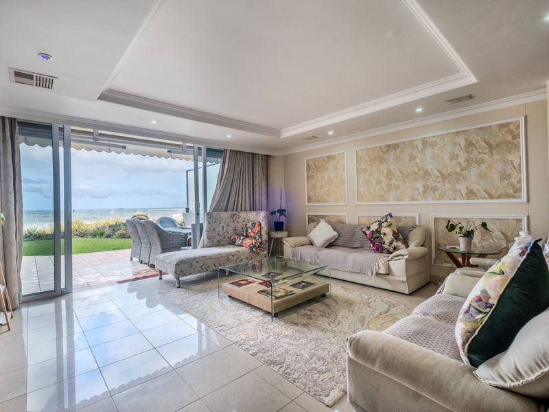 Spacious open-plan living area featuring elegant wall paneling, recessed ceiling details, and large sliding glass doors opening to a patio with ocean views.