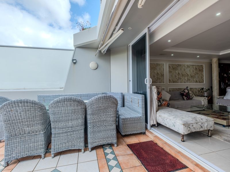A spacious balcony featuring tiled flooring, a retractable awning, and seamless indoor-outdoor flow through large sliding glass doors into the living area.