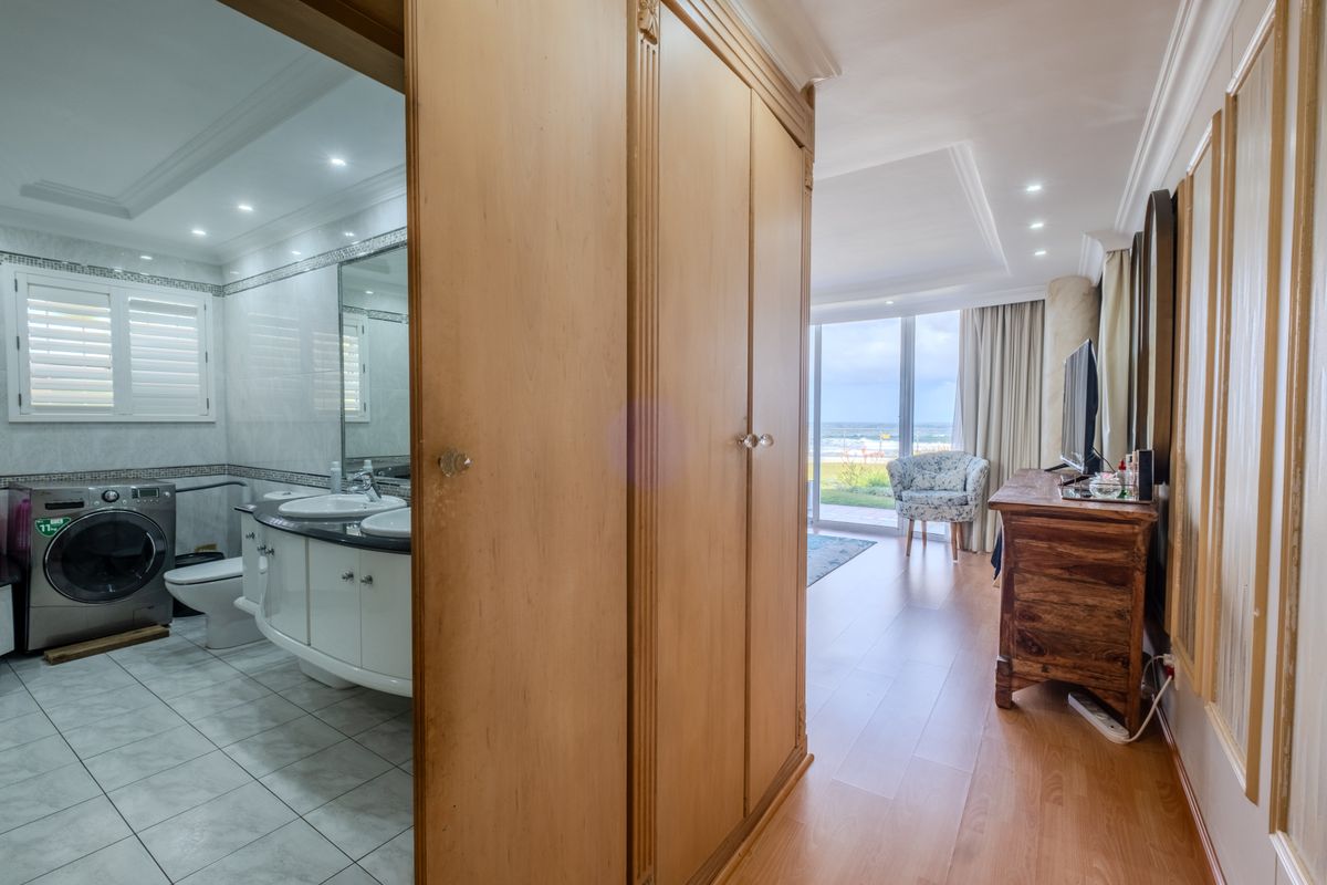 A bedroom featuring laminate flooring, built-in wardrobes, and an en-suite bathroom with a double vanity and integrated laundry facilities, leading to a balcony.