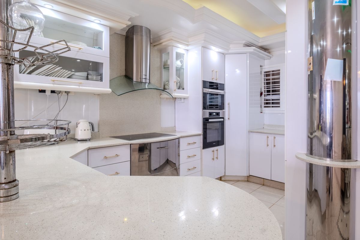 Modern kitchen featuring white cabinetry, quartz countertops, integrated appliances including an oven and microwave, and a stainless steel extractor fan.