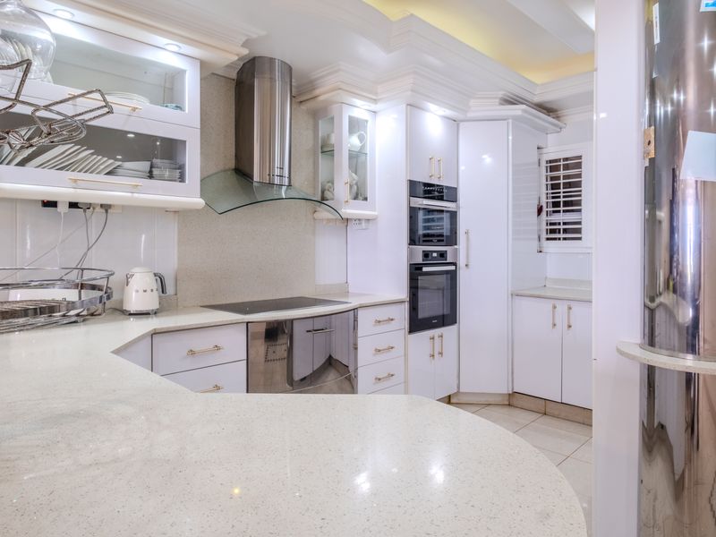 Modern kitchen featuring white cabinetry, quartz countertops, integrated appliances including an oven and microwave, and a stainless steel extractor fan.