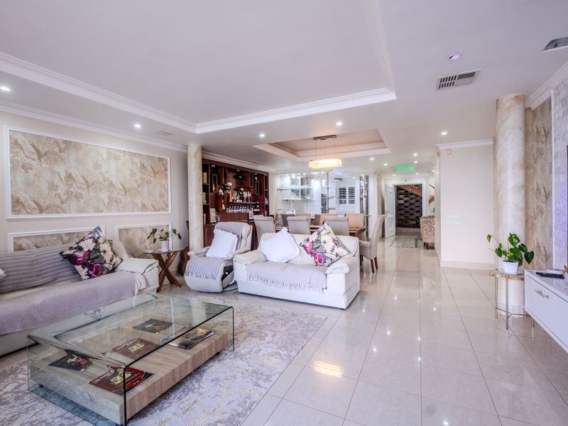 Spacious open-plan living and dining area featuring polished floor tiles, decorative wall finishes, recessed ceiling lighting, and a built-in bar unit.