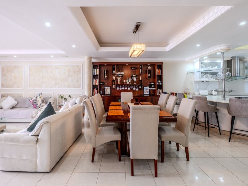 Spacious open-plan living and dining area featuring tiled floors, recessed ceiling details, a built-in bar unit, and a modern kitchen with a breakfast bar.