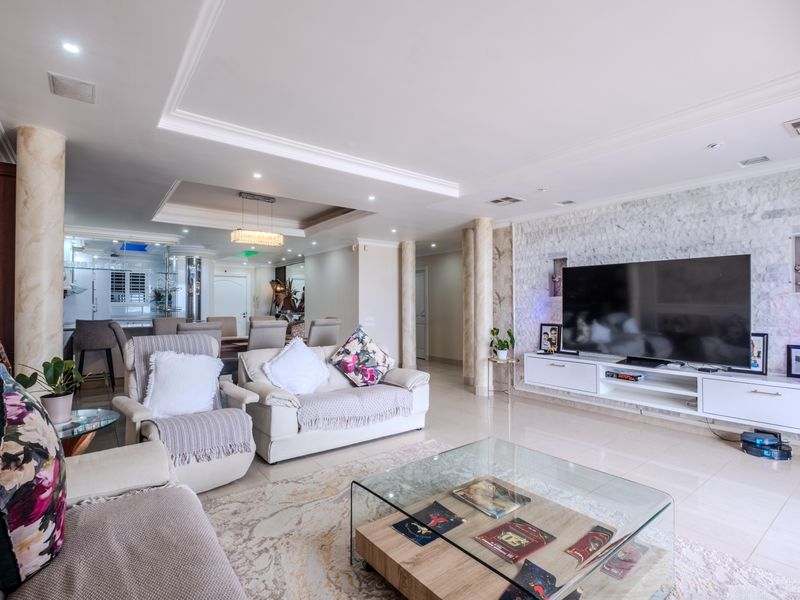 Spacious open-plan living area featuring a stone feature wall, recessed ceiling lighting, decorative columns, and polished tiled flooring.