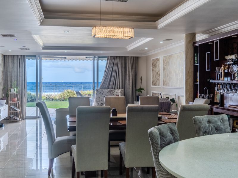 Spacious open-plan living and dining area featuring a tray ceiling, built-in bar, and large sliding doors opening to a scenic ocean view.