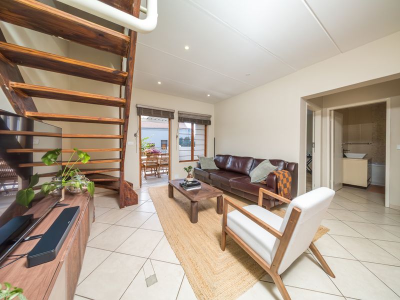 Open-plan living area featuring tiled flooring, an open-tread timber staircase, and direct access to an outdoor patio area.