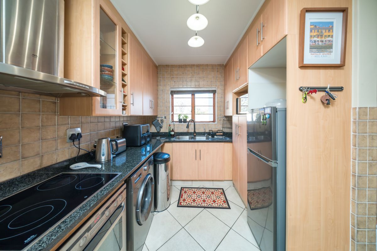 A functional galley-style kitchen featuring light wood cabinetry, granite countertops, integrated appliances, and a tiled backsplash with a window for natural light.