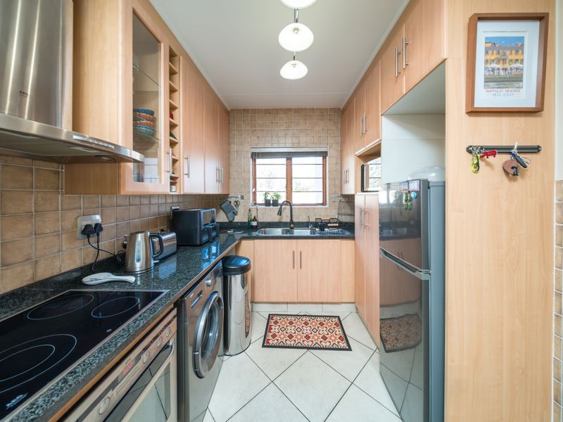 A functional galley-style kitchen featuring light wood cabinetry, granite countertops, integrated appliances, and a tiled backsplash with a window for natural light.