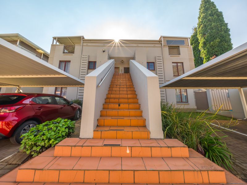 Front elevation of a townhouse complex featuring a central tiled staircase leading to upper units, flanked by covered carports and paved parking areas.