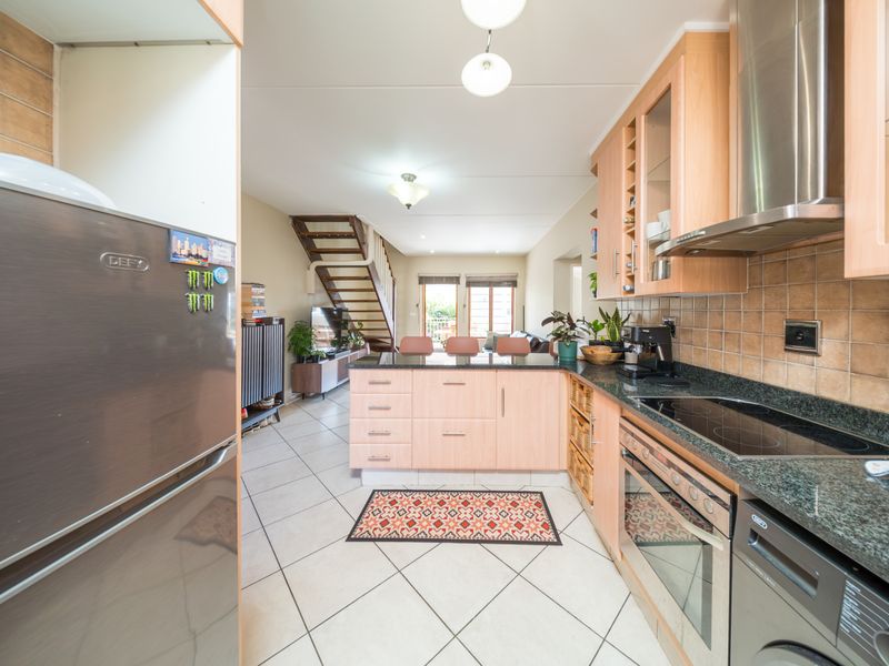Open-plan kitchen featuring light wood cabinetry, granite countertops, and integrated appliances, flowing seamlessly into the living area with a staircase.
