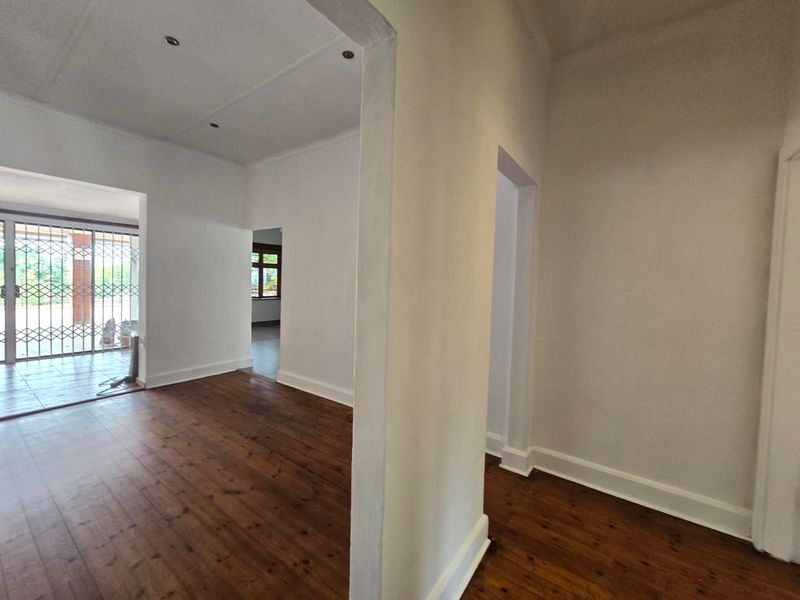 A bright, empty hallway featuring polished timber flooring, neutral walls, and recessed downlighting, leading into adjacent living spaces.