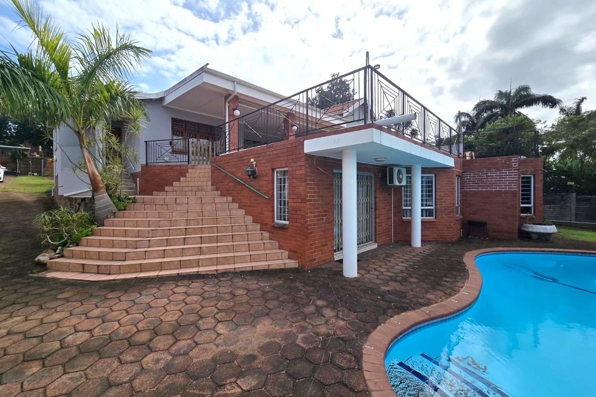 Rear exterior view featuring a swimming pool, paved patio area, brick facade, and a raised balcony with metal railings accessed by a tiled staircase.