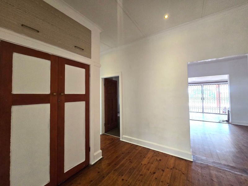 A bright hallway featuring original timber flooring, built-in storage cupboards, and a clear view through to the adjacent living area with security gates.
