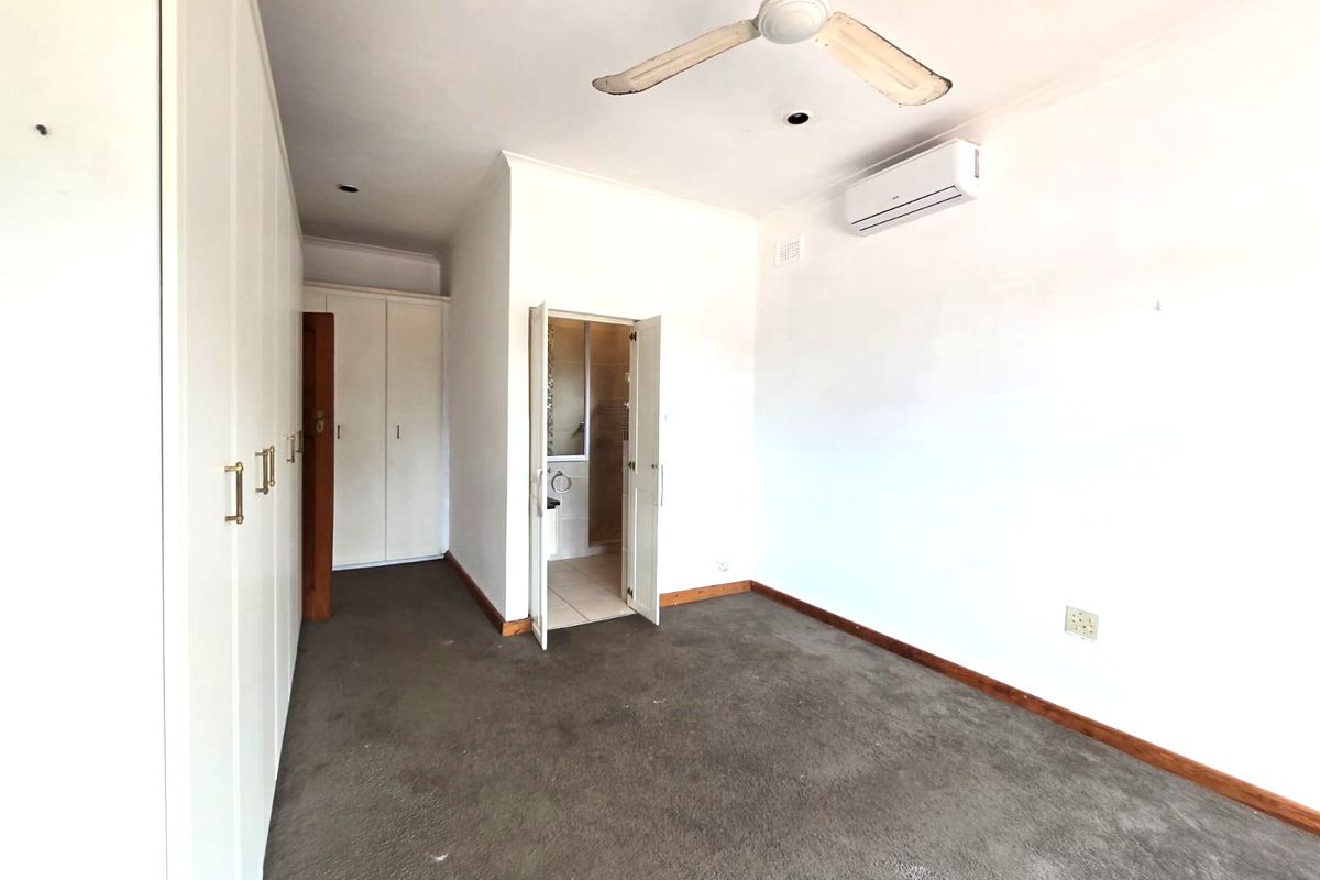 An empty bedroom featuring built-in cupboards, a ceiling fan, split-system air conditioning, and direct access to an en-suite bathroom.