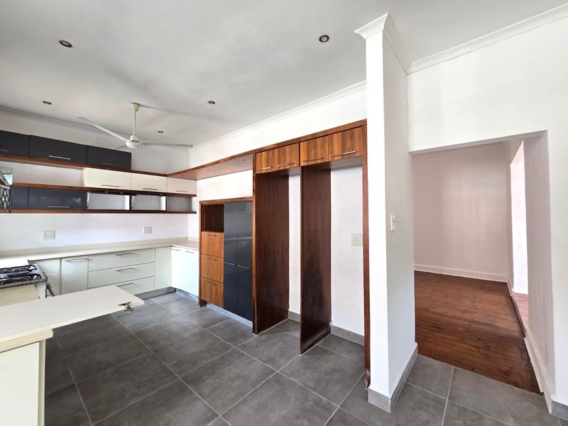 A spacious kitchen featuring modern two-tone cabinetry, built-in hob, and tiled flooring, with an adjacent room featuring warm laminate wood flooring.