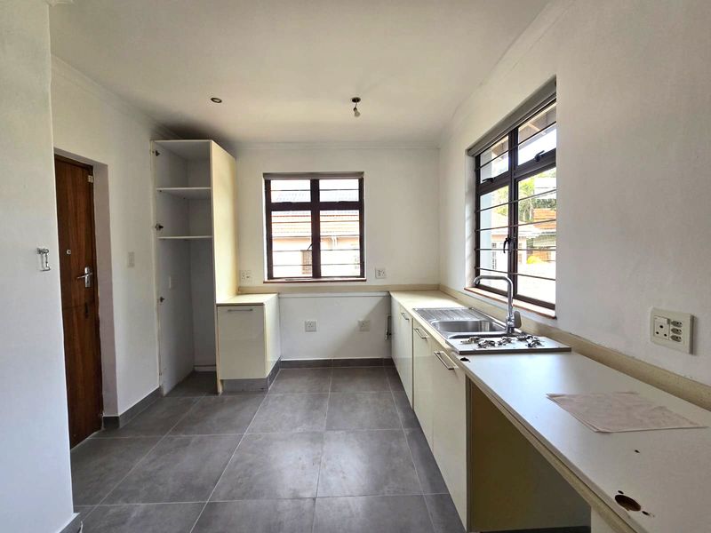 An empty kitchen featuring tiled floors, built-in cabinetry, and a stainless steel sink, awaiting final finishes and appliance installation.