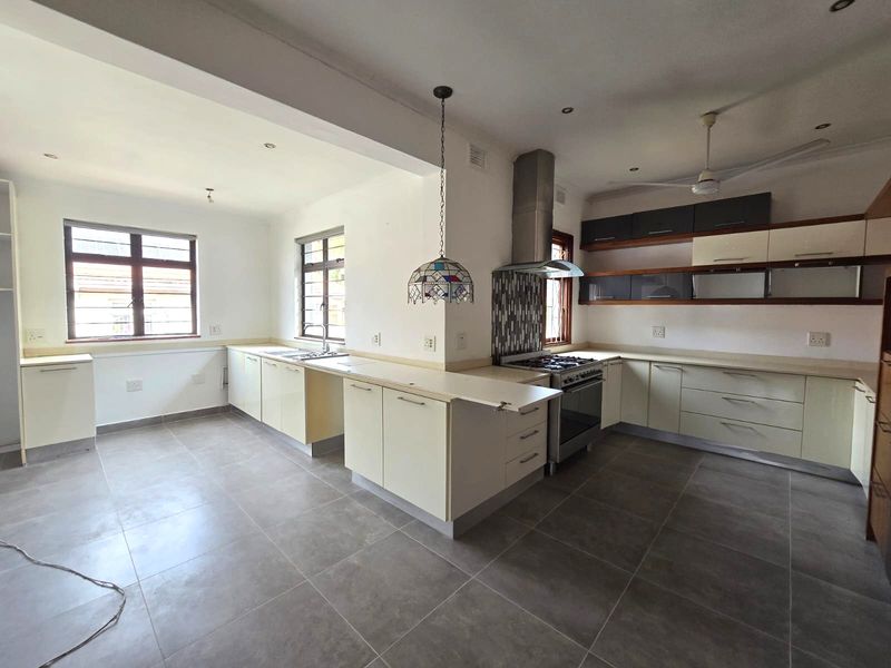 Spacious kitchen featuring neutral cabinetry, tiled flooring, a gas stove with extractor fan, and ample counter space.