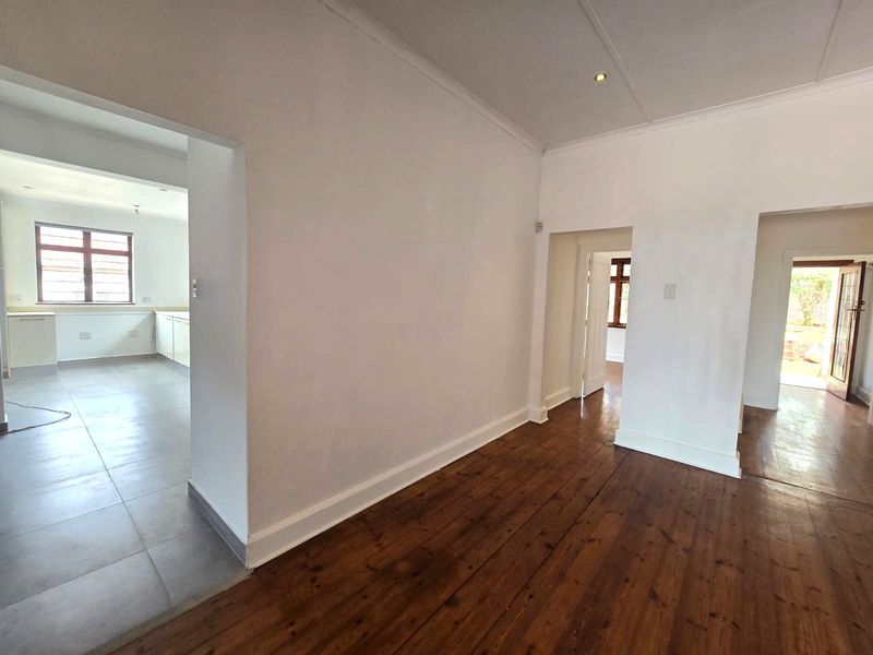 An empty living area featuring polished timber flooring, coved cornicing, and open access to an adjacent kitchen and hallway.