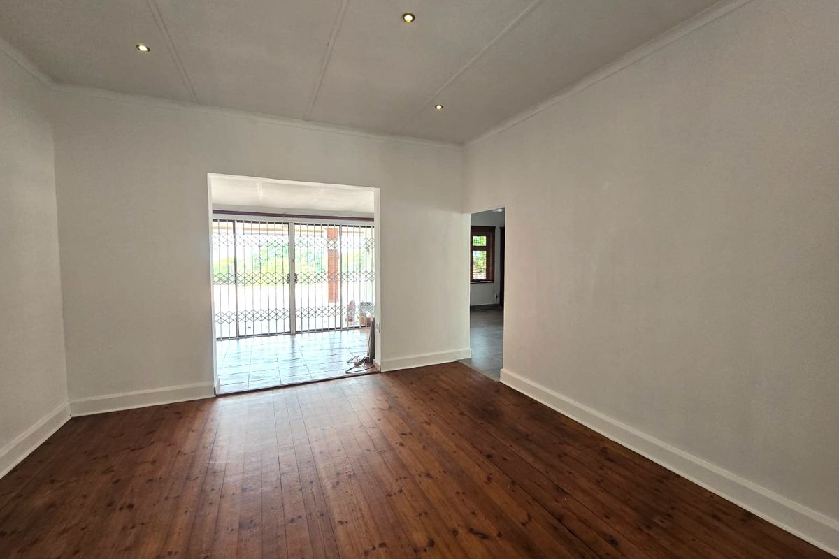A bright, empty living room featuring polished timber flooring, recessed downlighting, and a security gate leading to an outdoor patio area.
