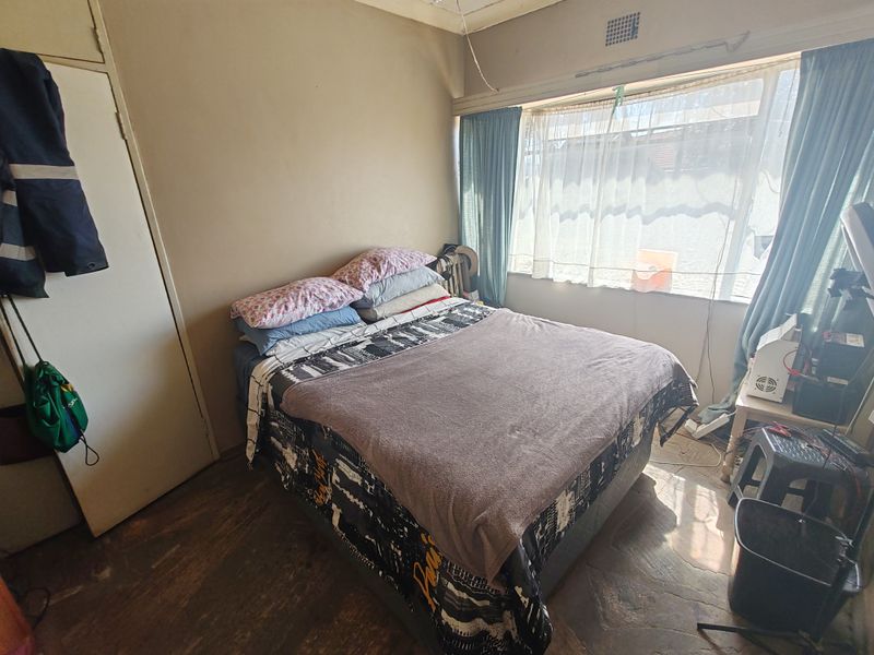 A bedroom featuring a built-in wardrobe and a large window, currently showing signs of wear including ceiling damage and exposed wiring.