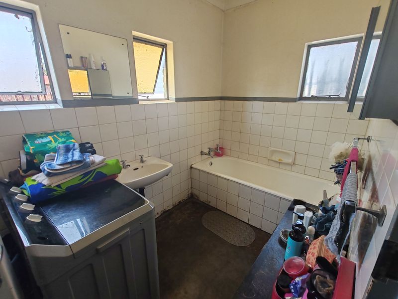 A dated bathroom featuring a bathtub, wall-mounted basin, and tiled walls, requiring renovation to update the finishes and improve the overall condition.