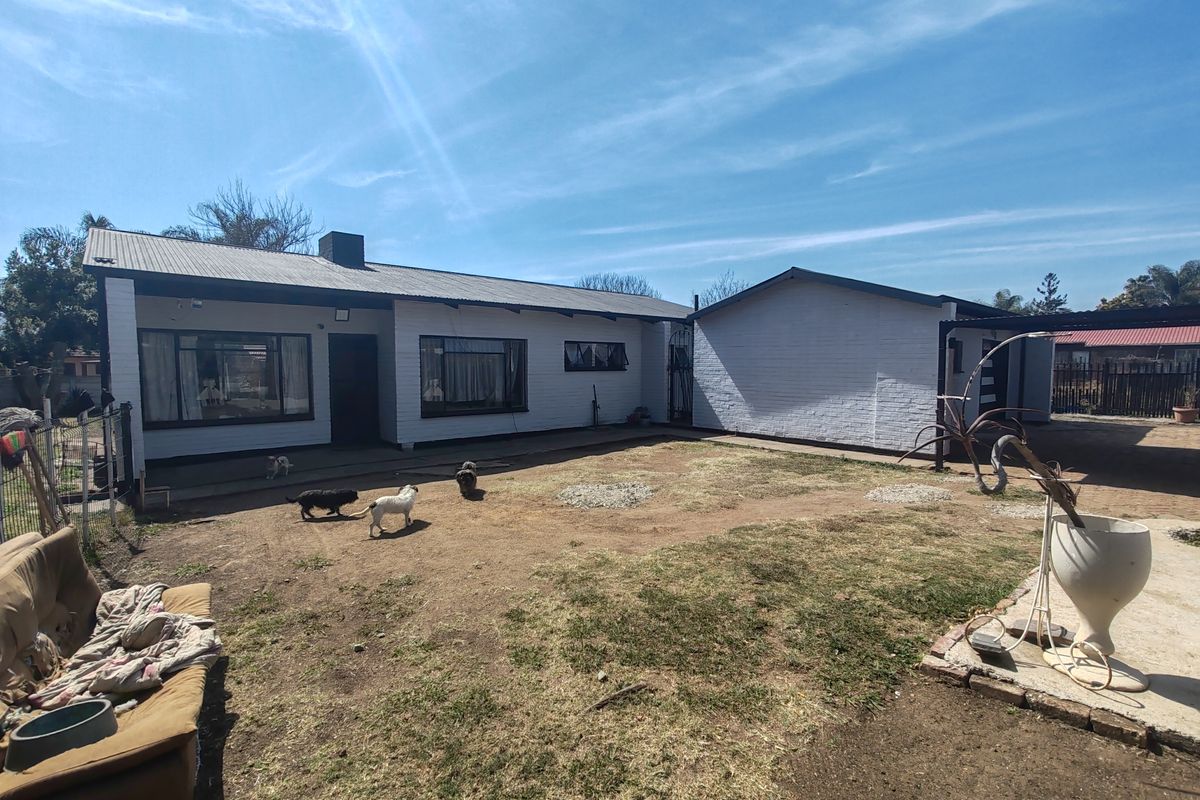 Rear view of a single-story house featuring a painted brick exterior, corrugated metal roof, and a spacious backyard area.
