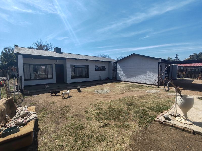 Rear view of a single-story house featuring a painted brick exterior, corrugated metal roof, and a spacious backyard area.