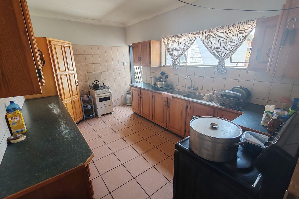 A functional kitchen featuring wooden cabinetry, tiled splashbacks, and a double sink, offering a dated aesthetic with potential for modern renovation.