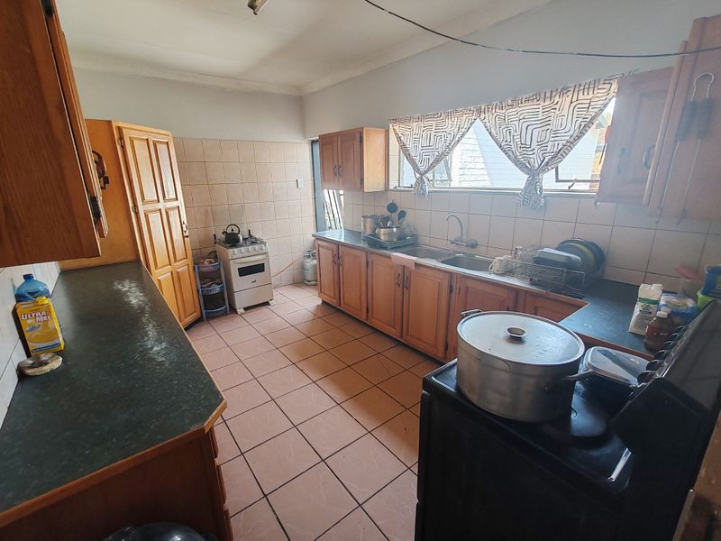 A functional kitchen featuring wooden cabinetry, tiled splashbacks, and a double sink, offering a dated aesthetic with potential for modern renovation.