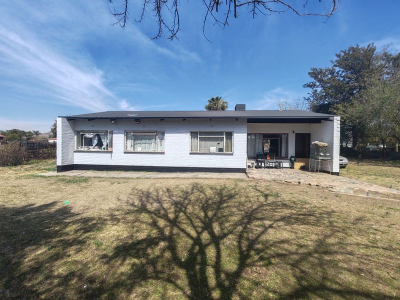 Rear view of a single-story brick house featuring a metal roof, stone patio area, and large windows overlooking a spacious garden.