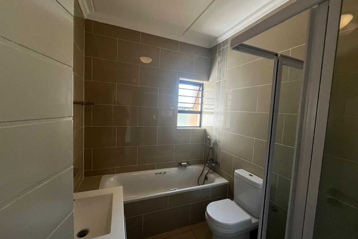 A clean, functional bathroom featuring a bathtub, separate shower enclosure, toilet, and vanity basin with neutral wall tiling.