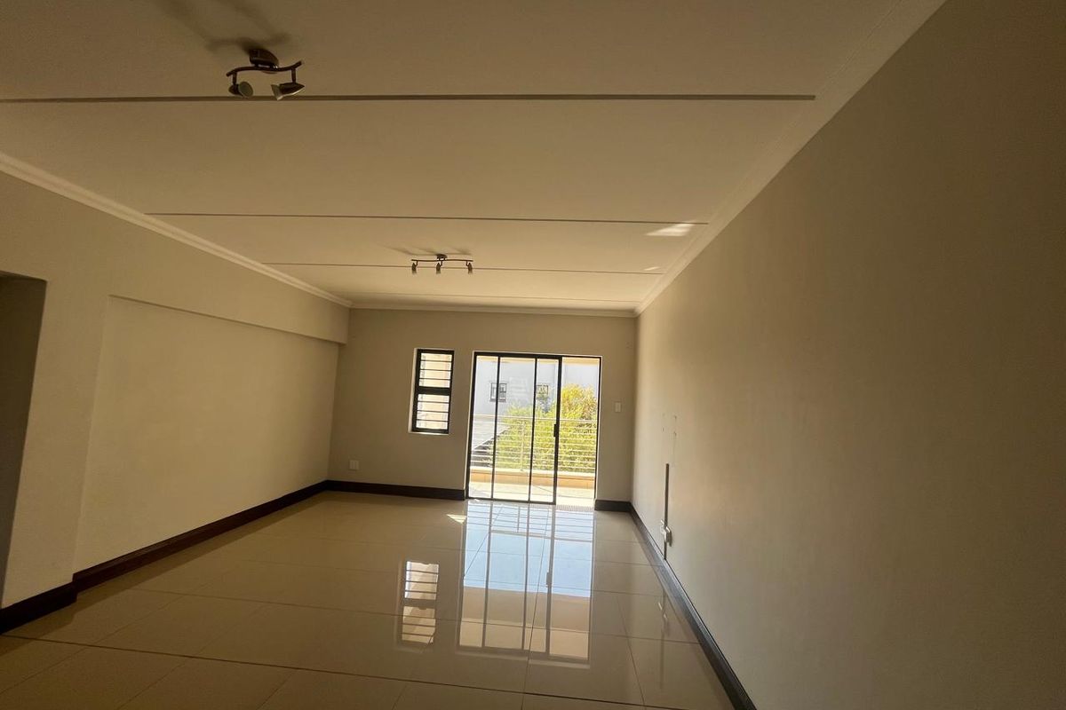 A spacious, empty living area featuring polished tile flooring, neutral walls, and a sliding glass door leading to an outdoor balcony.