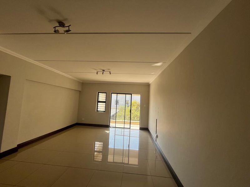 A spacious, empty living area featuring polished tile flooring, neutral walls, and a sliding glass door leading to an outdoor balcony.