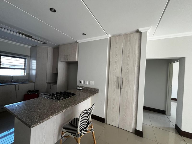 Modern kitchen featuring light wood-grain cabinetry, granite countertops, a built-in gas hob, and tiled flooring with ample storage space.