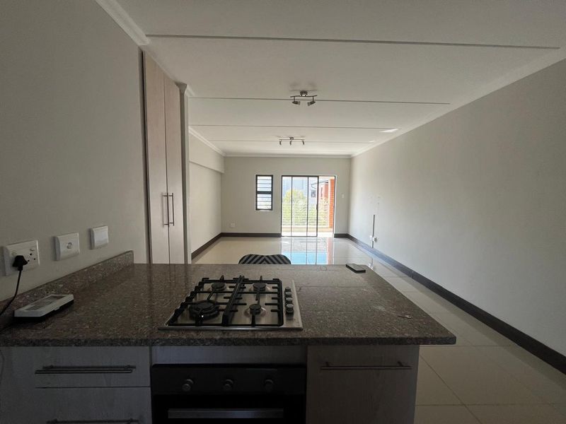Spacious open-plan living area featuring a modern kitchen with granite countertops, gas hob, built-in oven, and tiled flooring leading to a balcony.