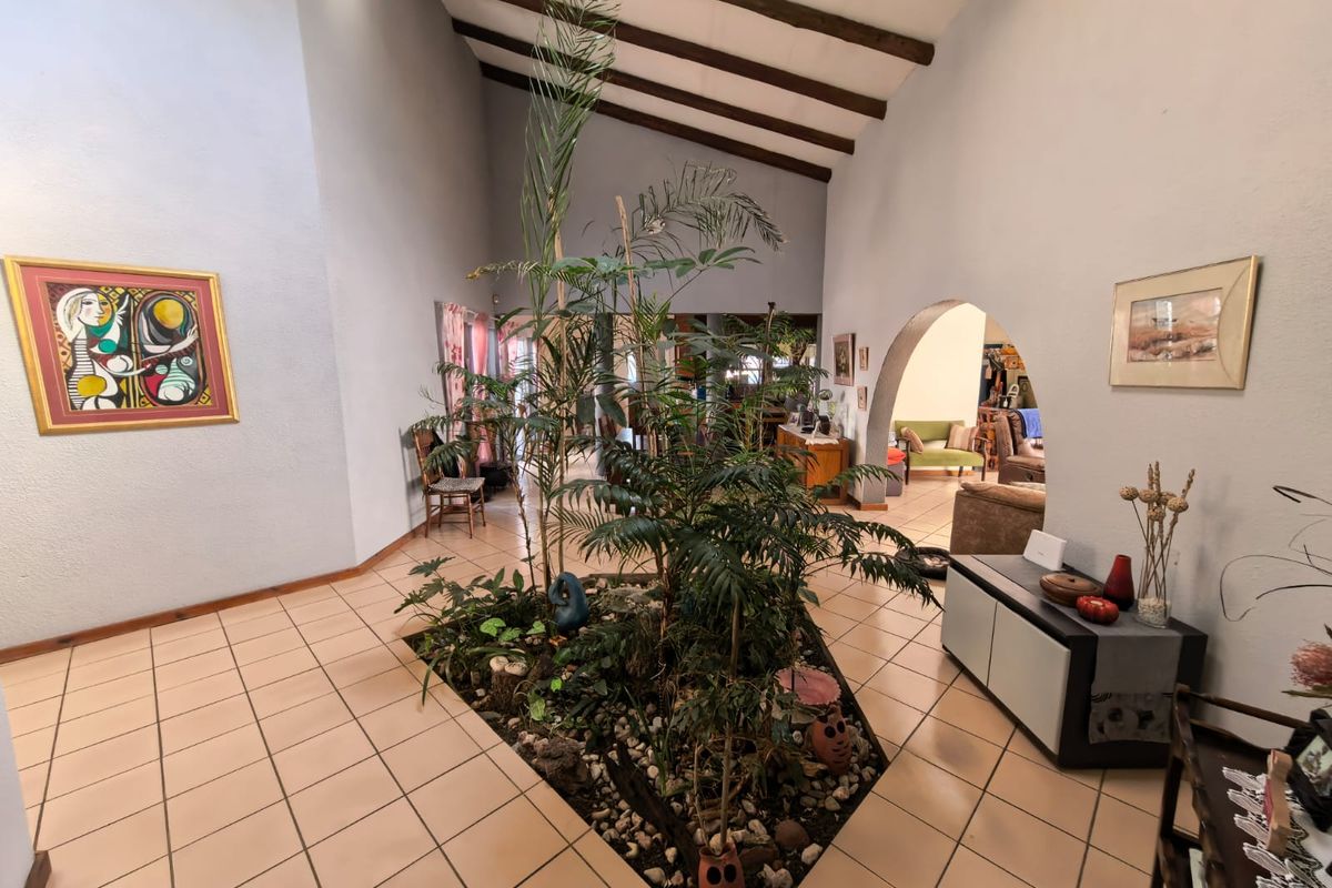 Spacious living area featuring a vaulted ceiling with exposed timber beams, ceramic tile flooring, and a unique central indoor garden feature.
