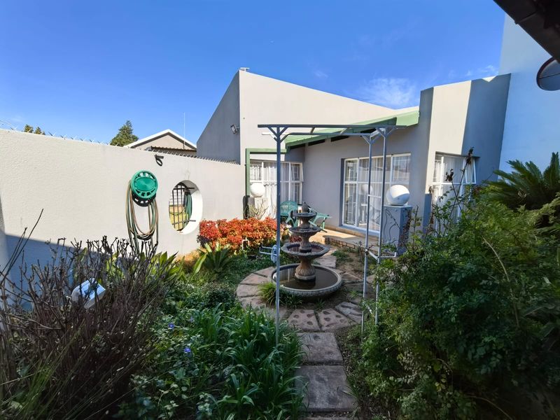 A rear garden area featuring a stone fountain, paved pathway, and access to the home via sliding glass doors, enclosed by a secure boundary wall.