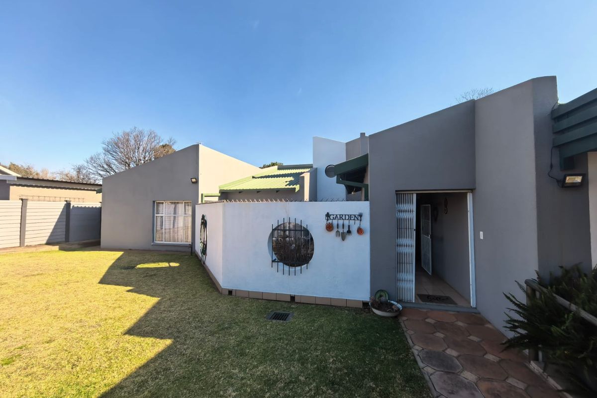 A well-maintained rear exterior view featuring a paved walkway, manicured lawn, and a secure entrance with a metal gate.
