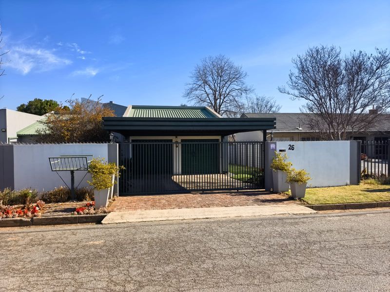 Front view of the property featuring a paved driveway, secure metal gate, carport, and perimeter walling.