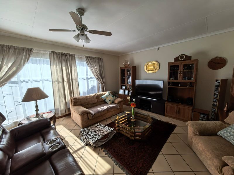 A comfortable living room featuring tiled flooring, a ceiling fan, and built-in cabinetry, offering a functional space with natural light from large windows.