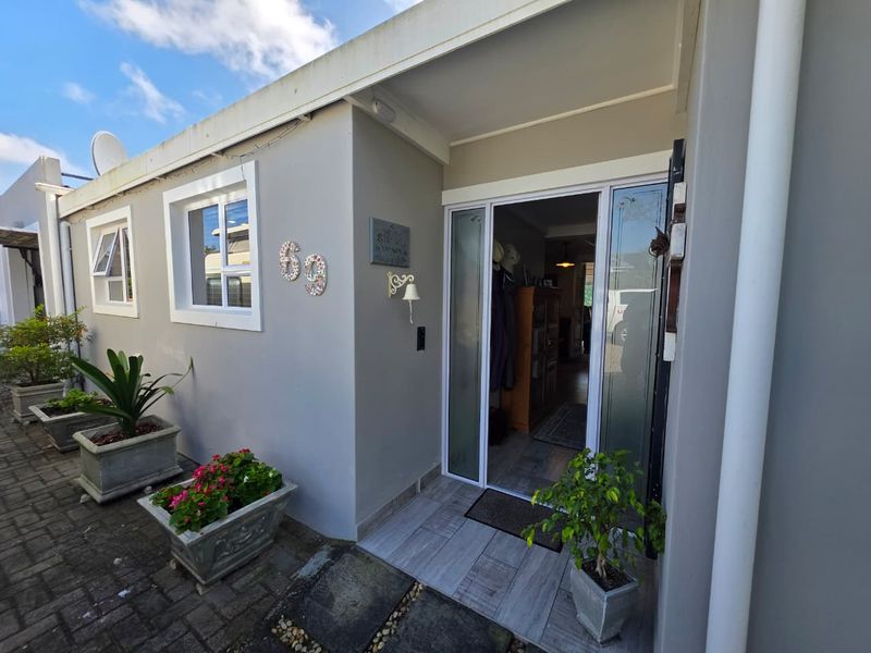 Front entrance of the house featuring a paved walkway, tiled porch area, and modern aluminium framed glass door.