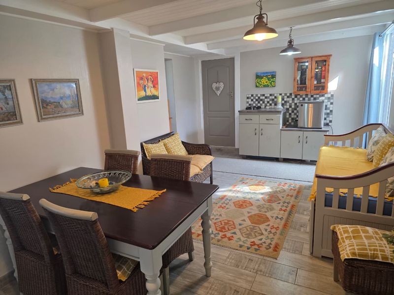 An open-plan living and kitchenette area featuring tiled flooring, exposed beam ceilings, and functional cabinetry with a tiled backsplash.