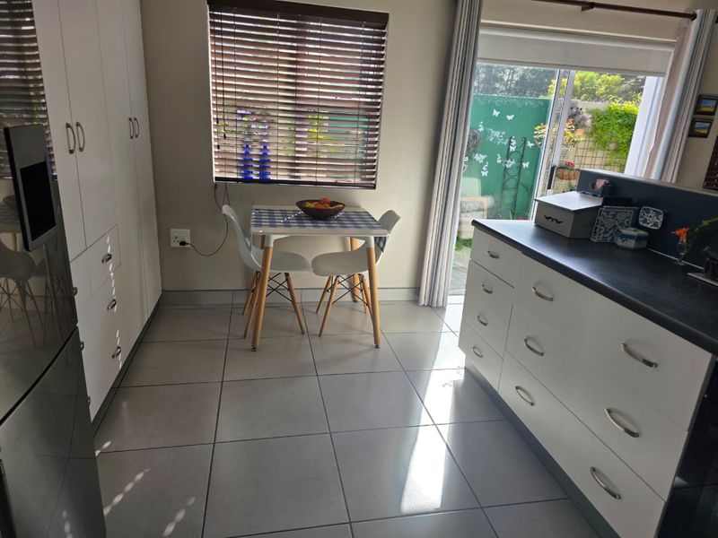 A functional kitchen area featuring white built-in cabinetry, dark countertops, tiled flooring, and direct access to an outdoor patio through a sliding glass door.