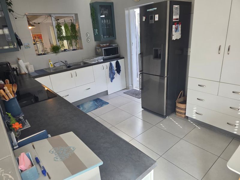 A functional kitchen featuring white cabinetry, dark laminate countertops, ceramic tile flooring, and a built-in pantry cupboard for ample storage.